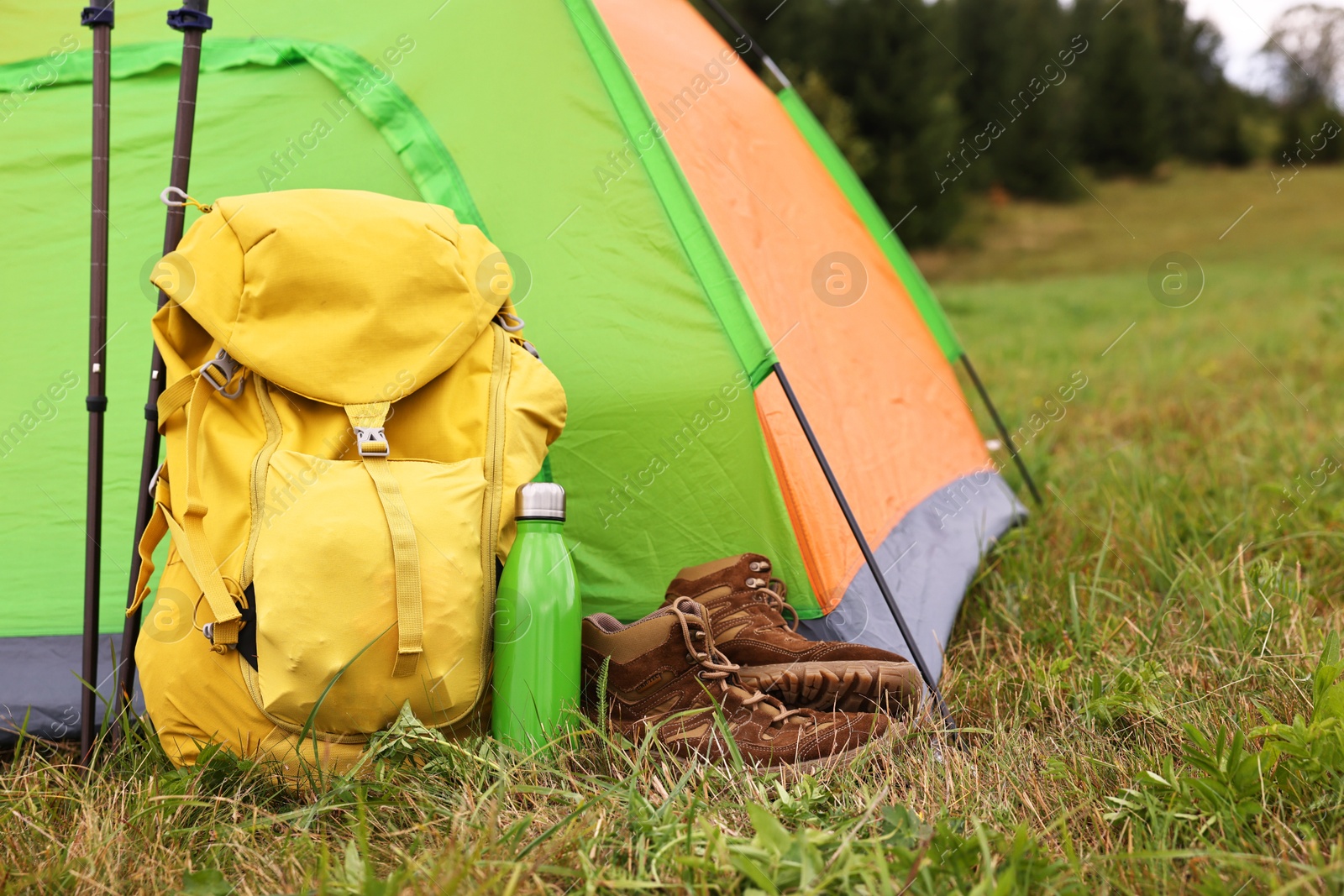 Photo of Tent, backpack, trekking poles and thermos on green grass in mountains