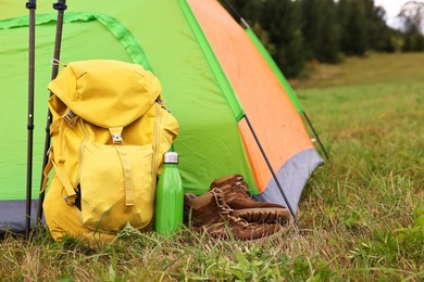 Tent, backpack, trekking poles and thermos on green grass in mountains