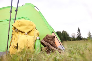 Tent, backpack, trekking poles and thermos on green grass in mountains