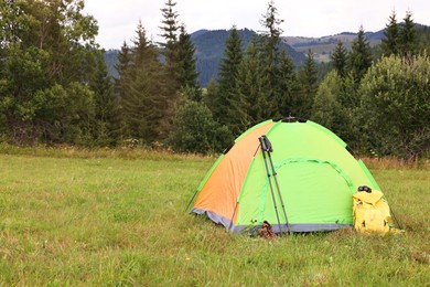 Tent, backpack and trekking poles on green grass in mountains