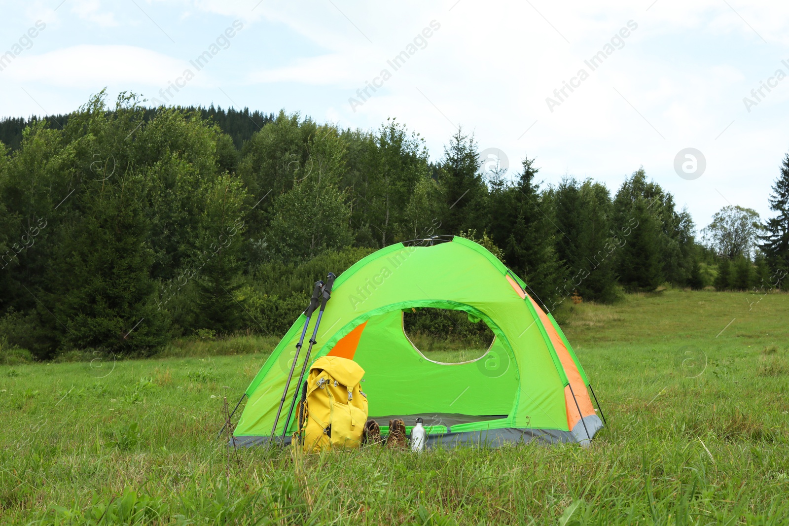 Photo of Tent, backpack and trekking poles on green grass in mountains