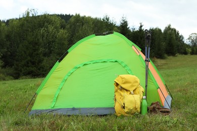 Photo of Tent, backpack and trekking poles on green grass in mountains