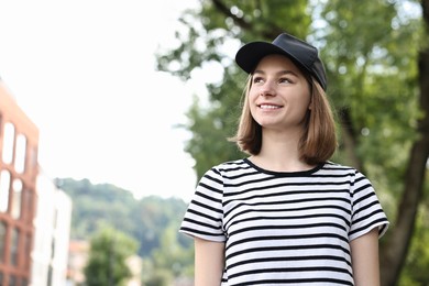 Portrait of smiling woman in baseball cap outdoors. Space for text