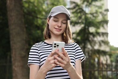 Smiling woman in baseball cap with smartphone outdoors