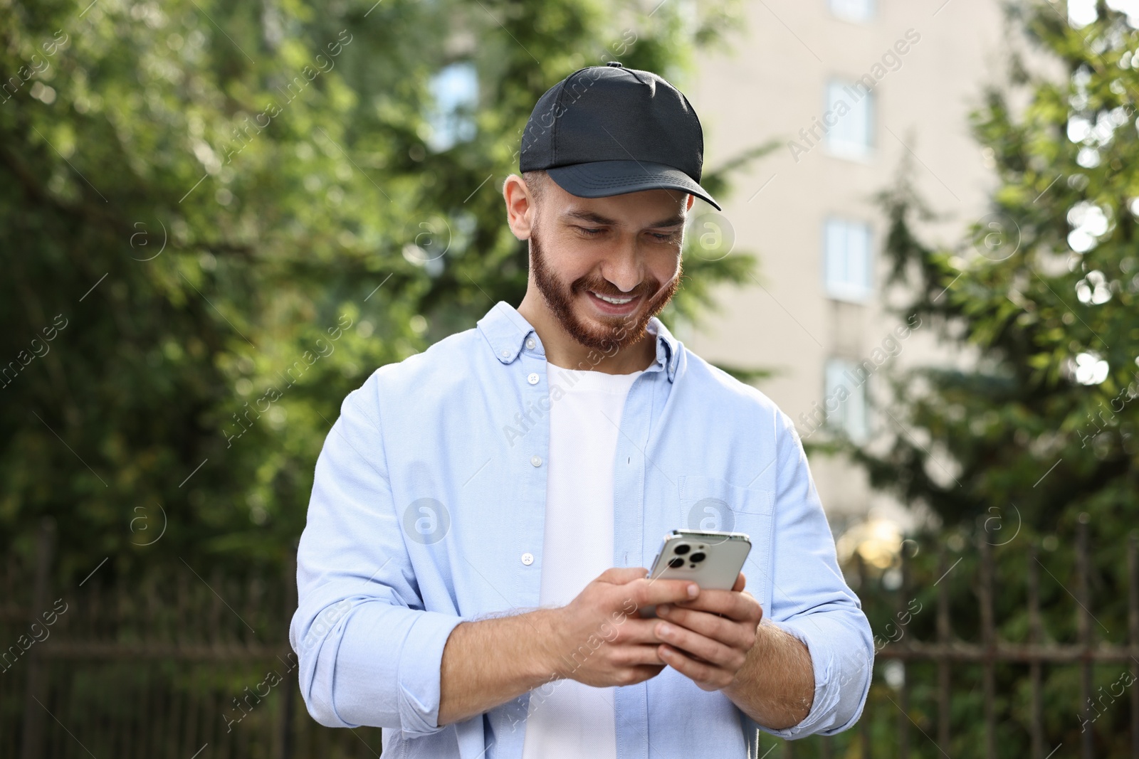 Photo of Smiling man in baseball cap with smartphone outdoors