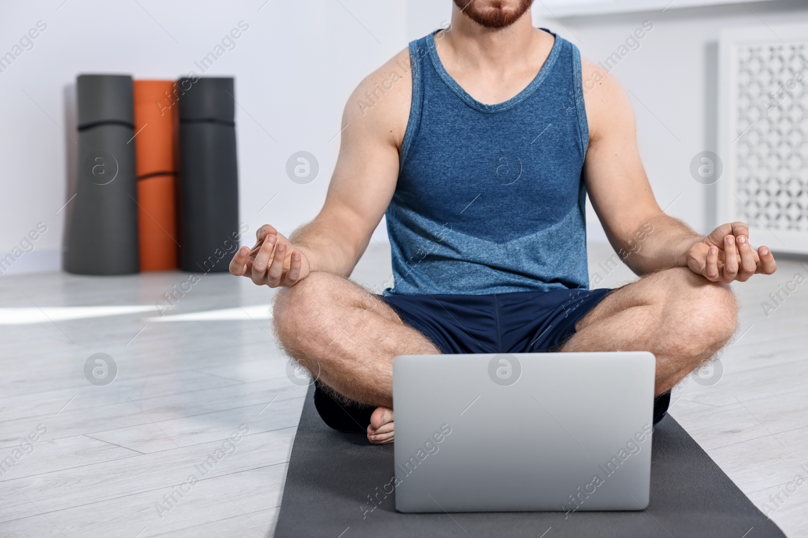 Photo of Man meditating near laptop on yoga mat at home, closeup. Space for text