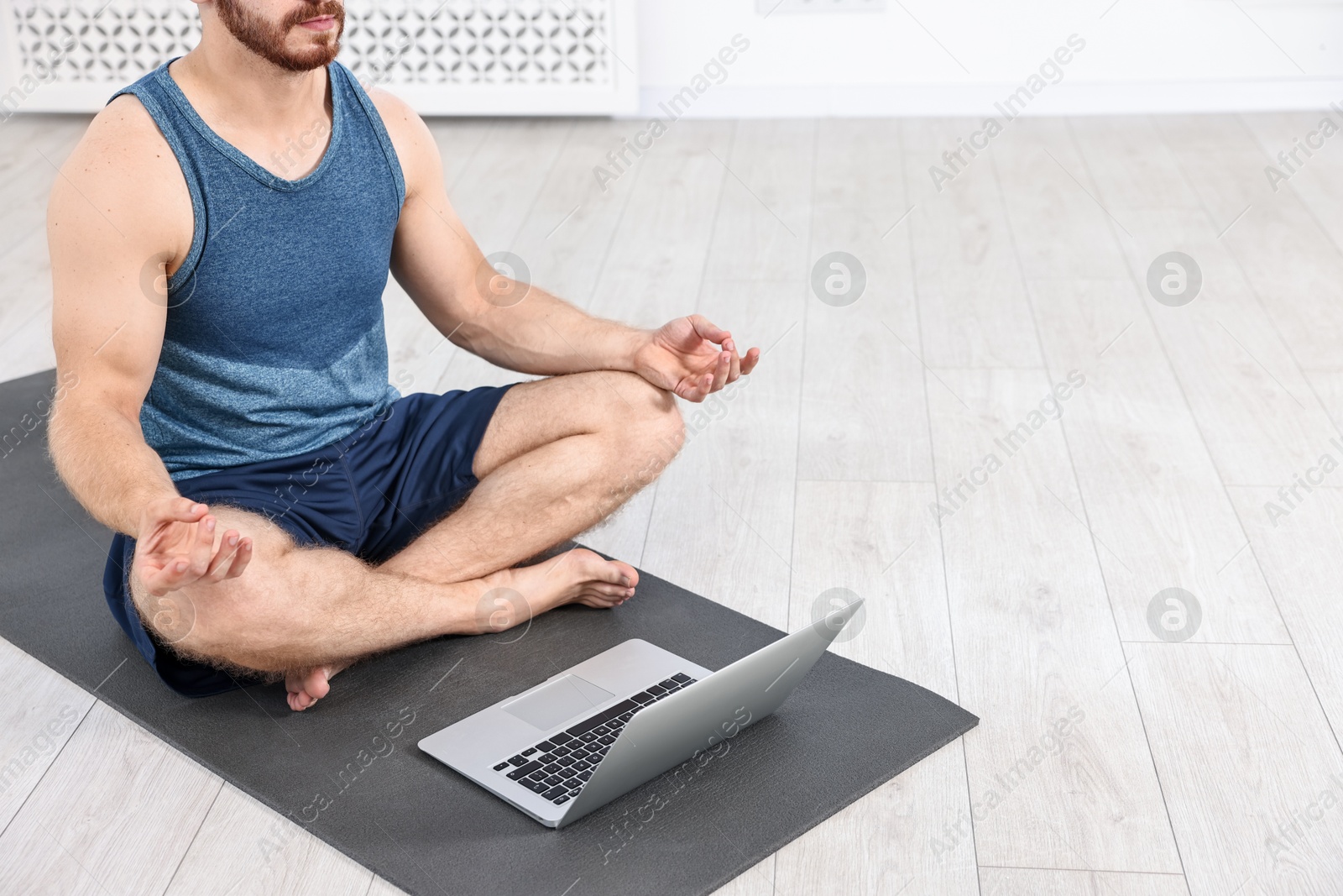 Photo of Man meditating near laptop on yoga mat at home, closeup. Space for text