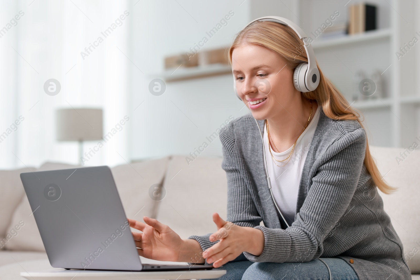 Photo of Interpreter in headphones having video chat via laptop on sofa at home