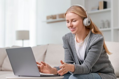 Interpreter in headphones having video chat via laptop on sofa at home