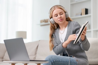 Interpreter in headphones having video chat via laptop on sofa at home