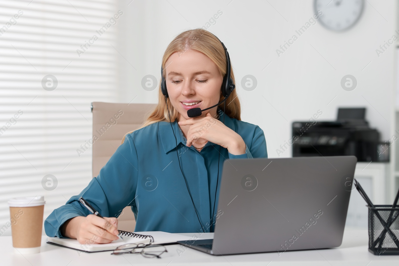 Photo of Interpreter in headset taking notes while working with laptop at table indoors