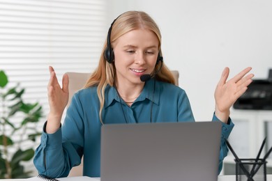 Interpreter in headset having video chat via laptop at table indoors