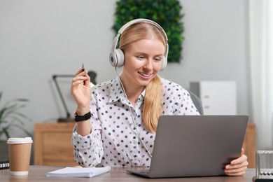 Interpreter in headphones working with laptop at table indoors