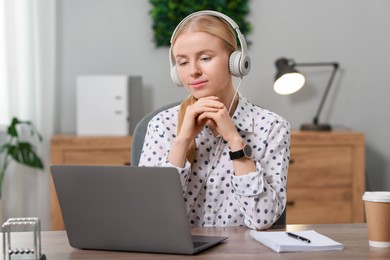 Photo of Interpreter in headphones working with laptop at table indoors