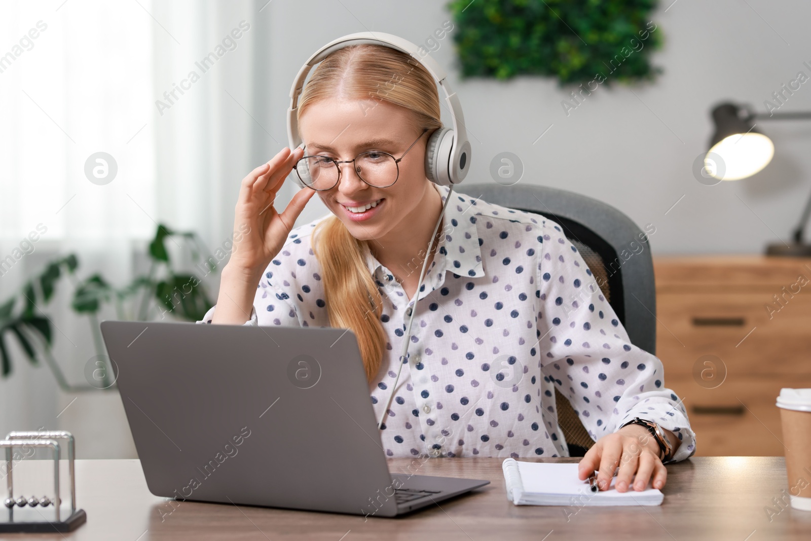 Photo of Interpreter in headphones working with laptop at table indoors