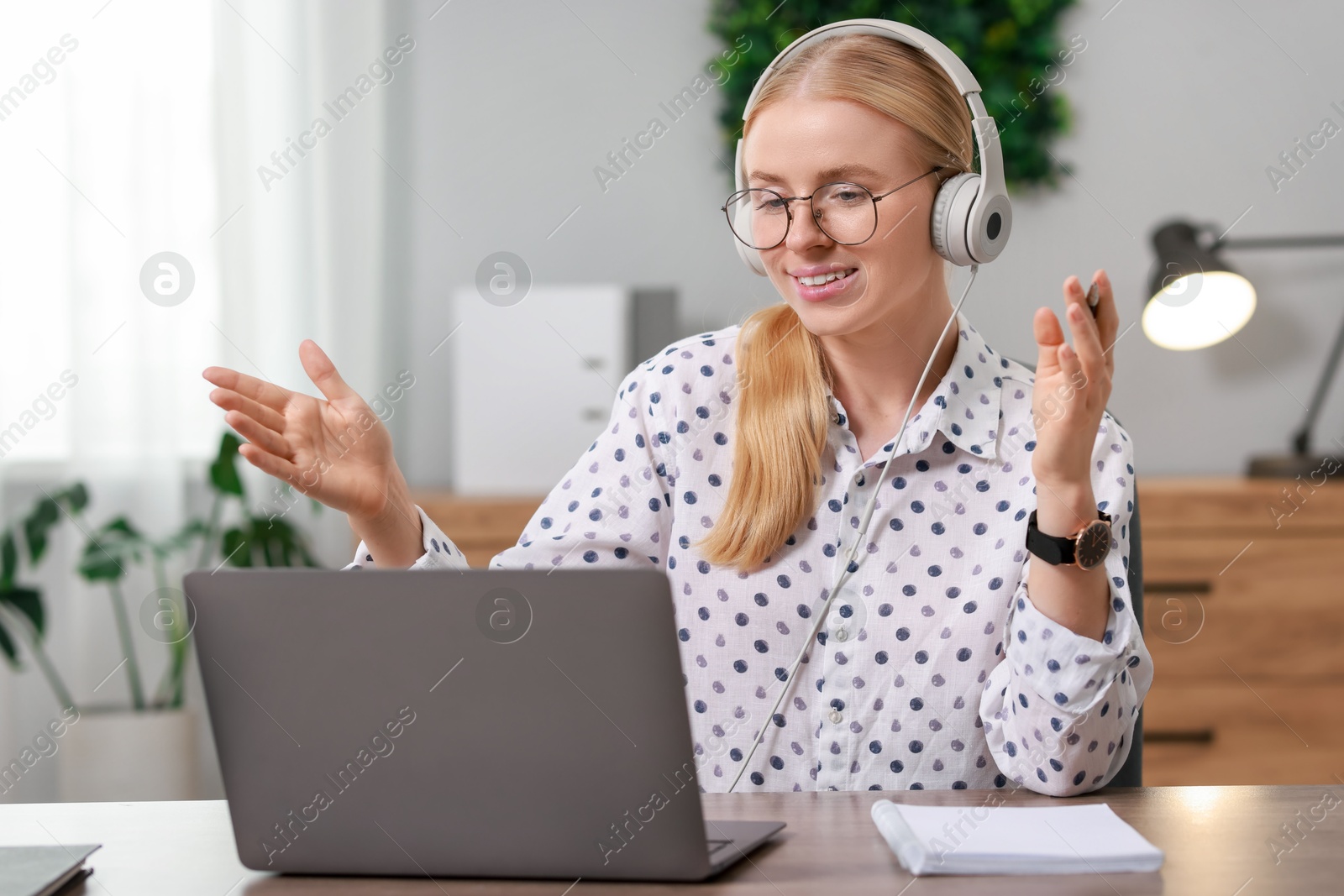 Photo of Interpreter in headphones having video chat via laptop at table indoors