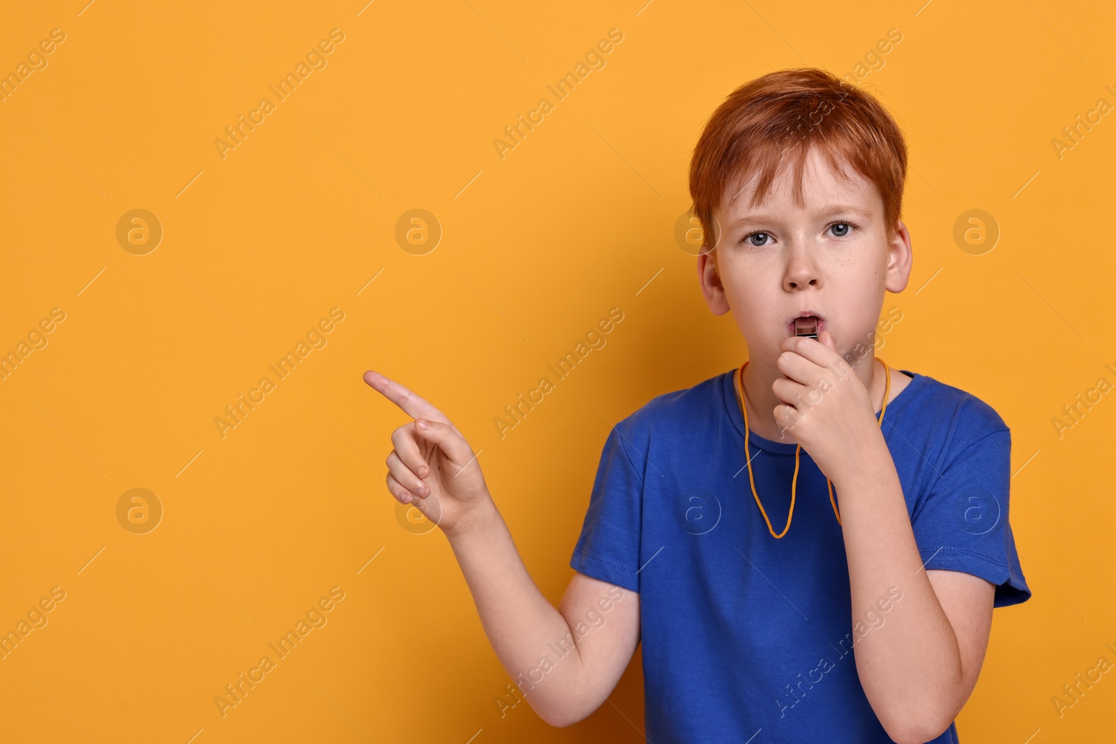 Photo of Little boy blowing whistle on orange background, space for text