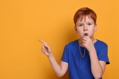 Little boy blowing whistle on orange background, space for text