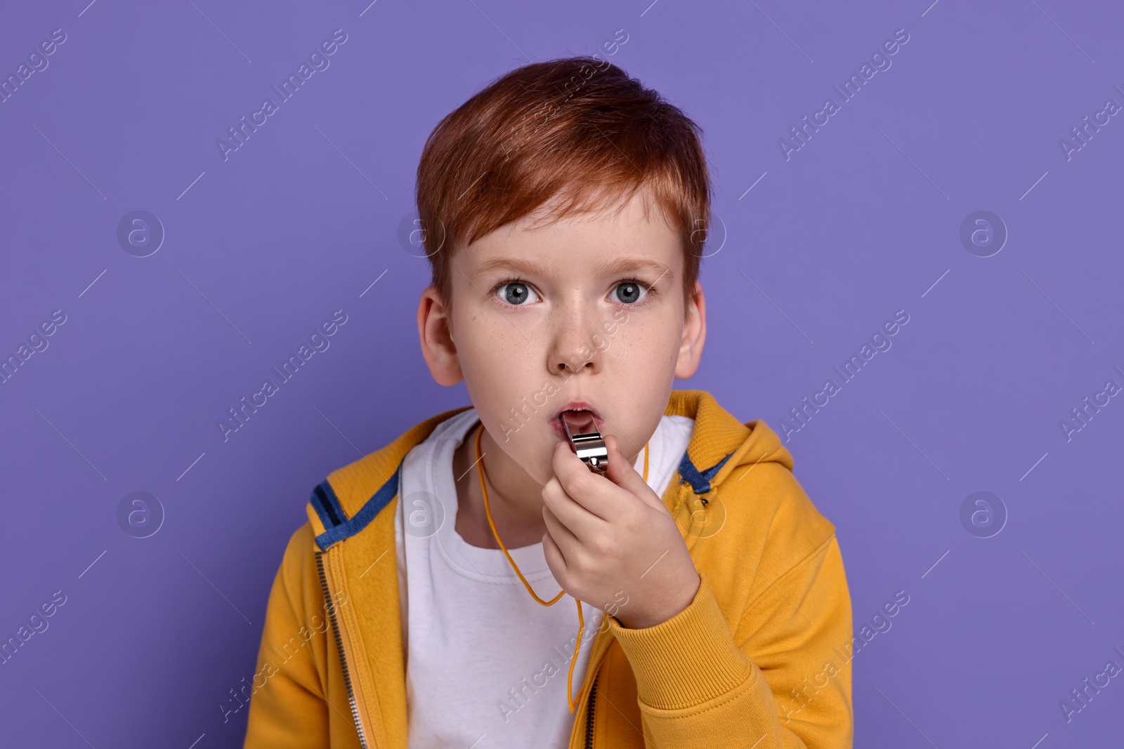 Photo of Little boy blowing whistle on purple background