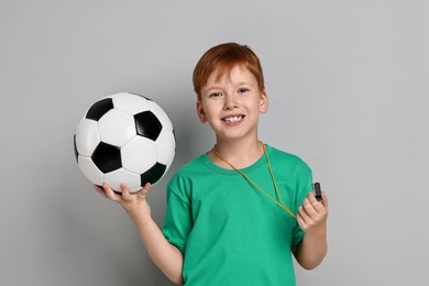 Little boy with whistle and soccer ball on grey background