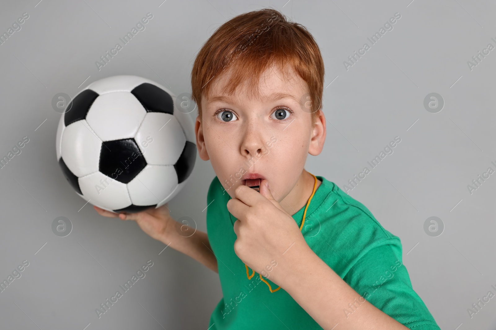 Photo of Little boy with soccer ball blowing whistle on grey background