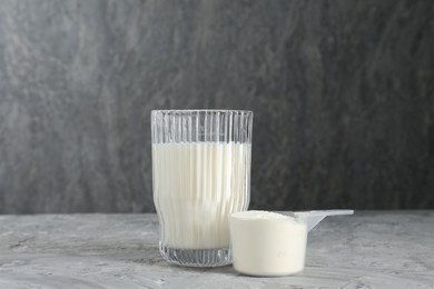 Photo of Delicious protein shake in glass and scoop with powder on gray textured table