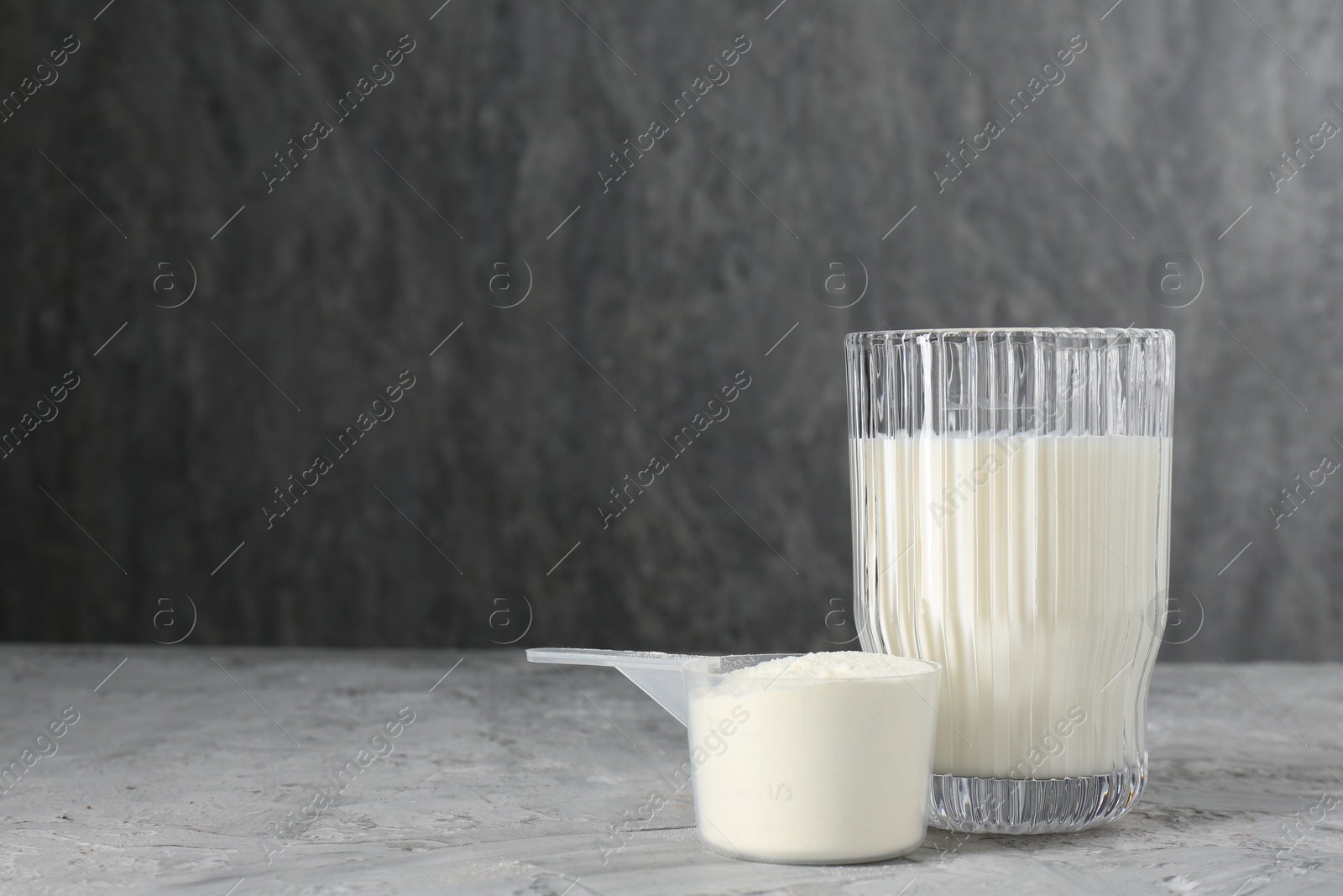 Photo of Delicious protein shake in glass and scoop with powder on gray textured table, space for text