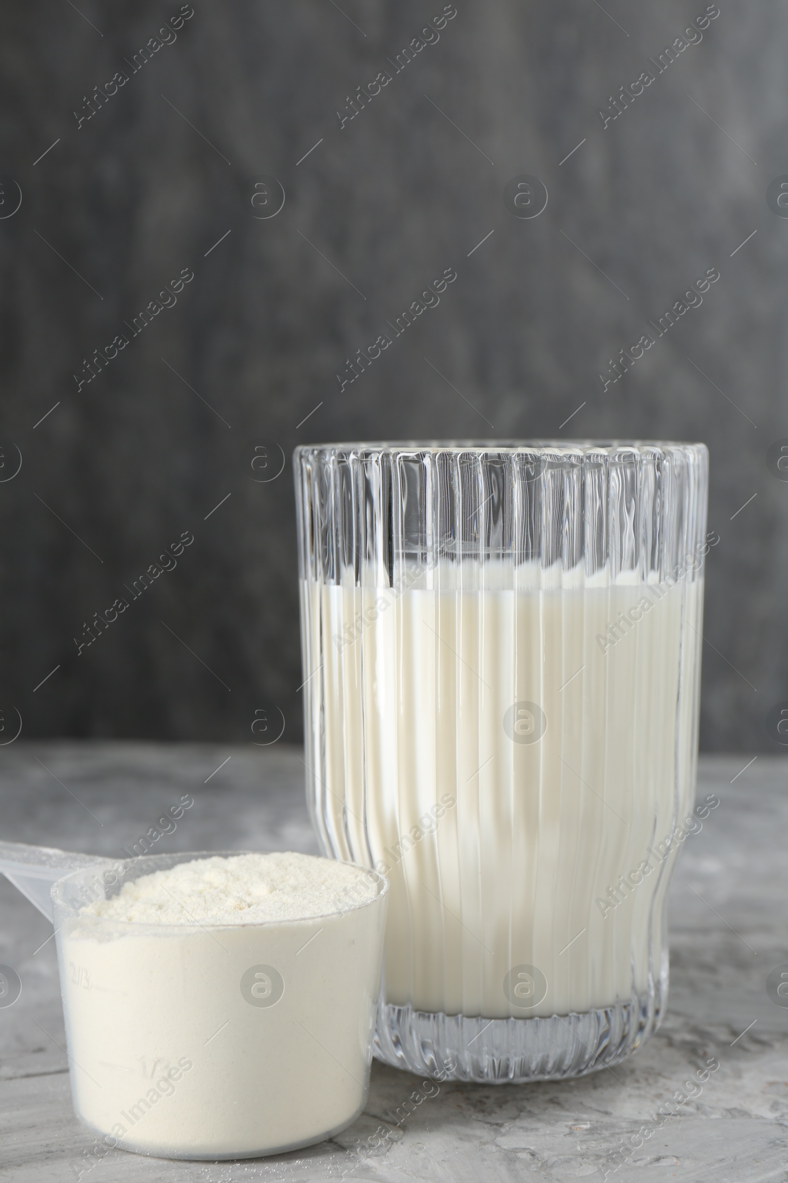 Photo of Delicious protein shake in glass and scoop with powder on gray textured table