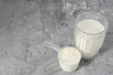 Photo of Delicious protein shake in glass and scoop with powder on gray textured table, space for text