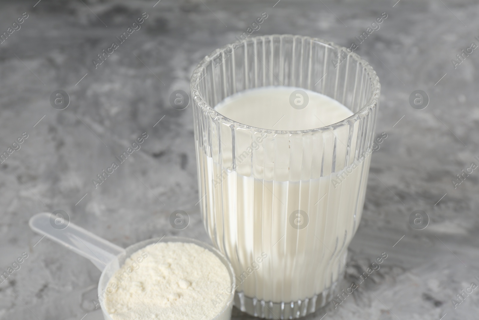 Photo of Delicious protein shake in glass and scoop with powder on gray textured table, closeup