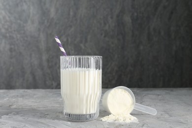 Photo of Delicious protein shake in glass and scoop with powder on gray textured table