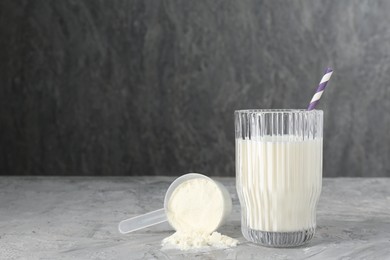 Photo of Delicious protein shake in glass and scoop with powder on gray textured table, space for text