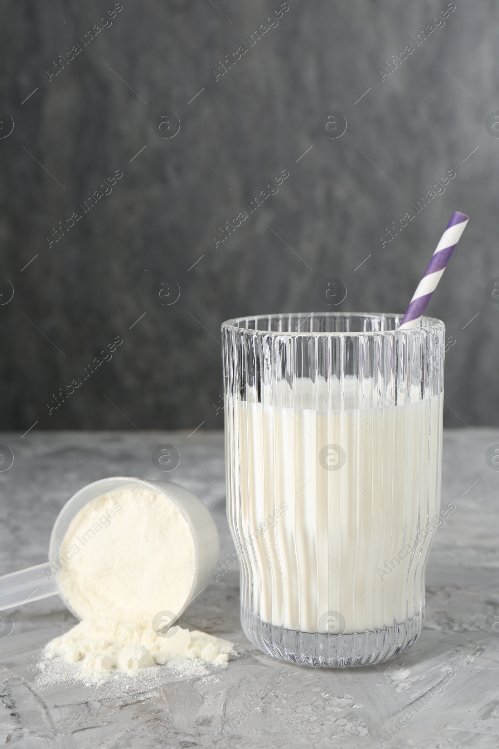 Photo of Delicious protein shake in glass and scoop with powder on gray textured table