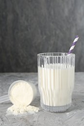 Photo of Delicious protein shake in glass and scoop with powder on gray textured table