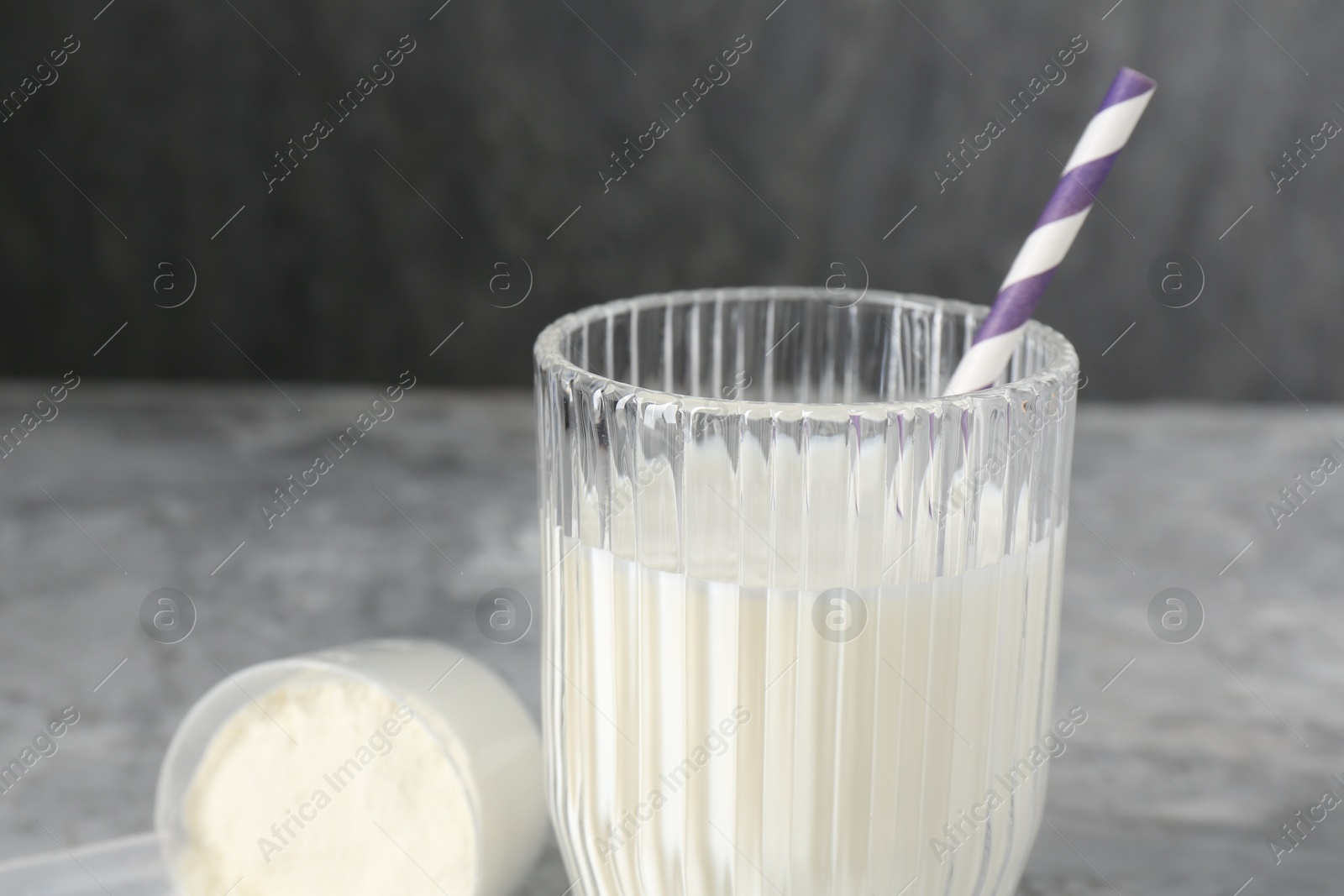 Photo of Delicious protein shake in glass and scoop with powder on gray table, closeup