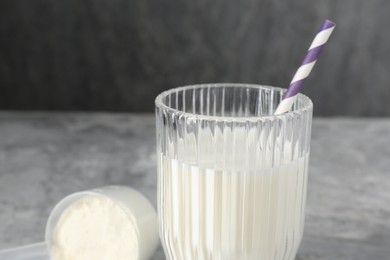 Photo of Delicious protein shake in glass and scoop with powder on gray table, closeup