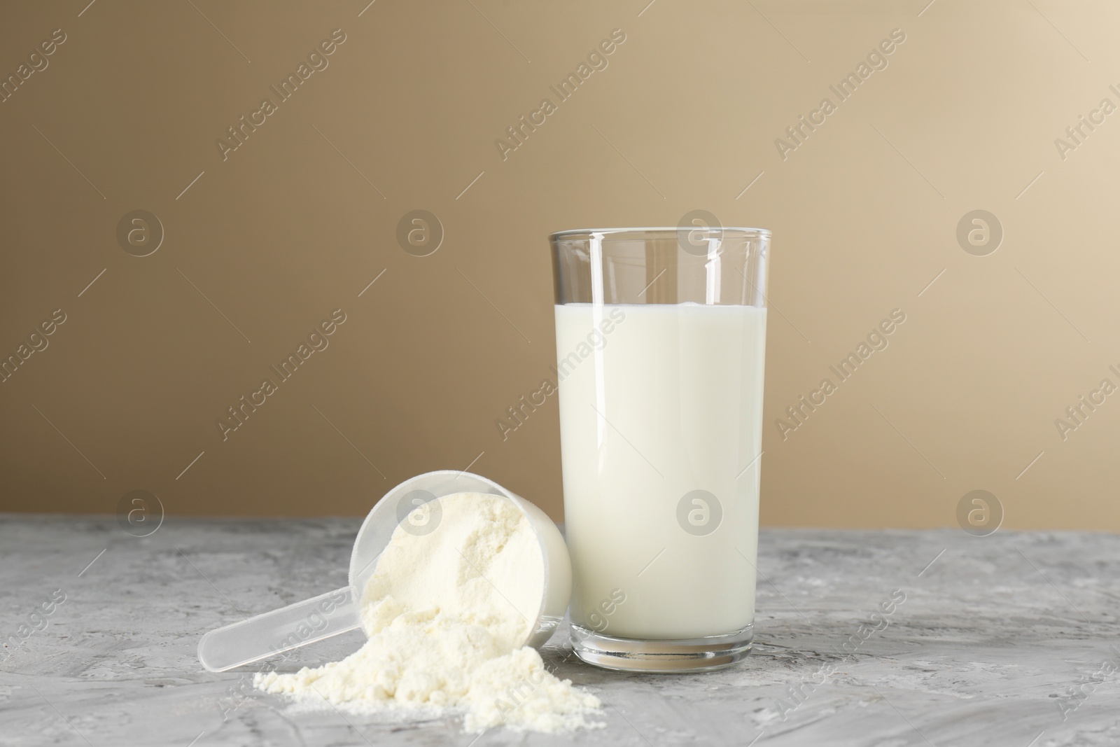 Photo of Delicious protein shake in glass and scoop with powder on gray textured table against beige background