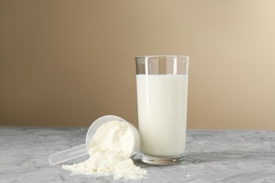 Photo of Delicious protein shake in glass and scoop with powder on gray textured table against beige background