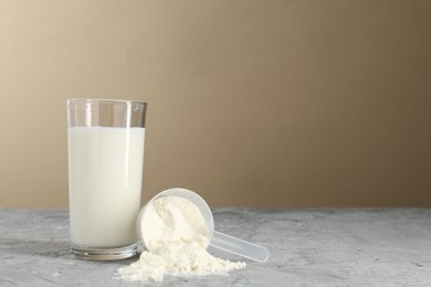 Photo of Delicious protein shake in glass and scoop with powder on gray textured table against beige background, space for text