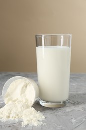 Photo of Delicious protein shake in glass and scoop with powder on gray textured table against beige background