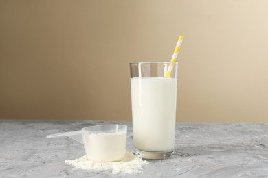 Photo of Delicious protein shake in glass and scoop with powder on gray textured table against beige background