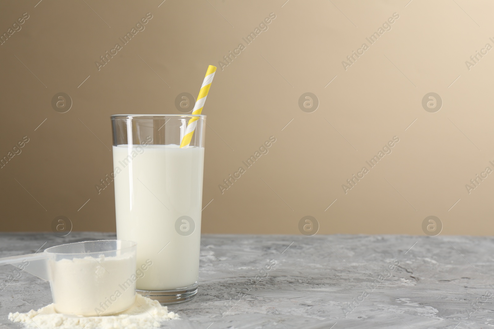 Photo of Delicious protein shake in glass and scoop with powder on gray textured table against beige background, space for text