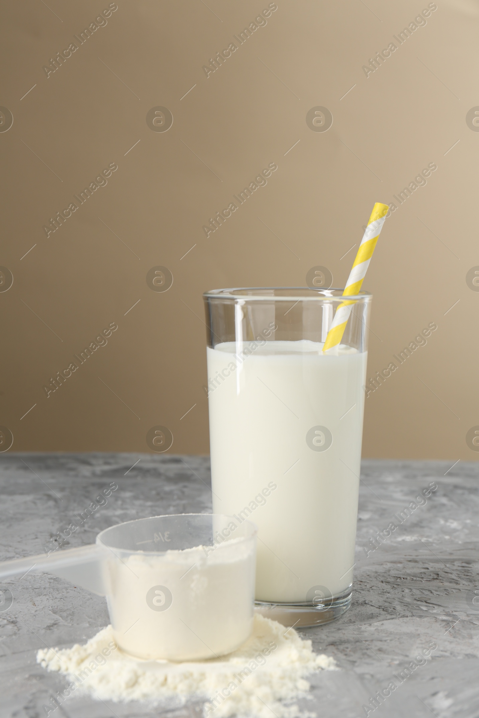 Photo of Delicious protein shake in glass and scoop with powder on gray textured table against beige background