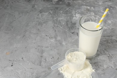 Photo of Delicious protein shake in glass and scoop with powder on gray textured table, space for text