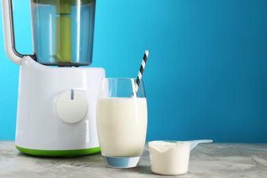 Photo of Blender, delicious protein shake in glass and scoop with powder on gray textured table against light blue background, space for text