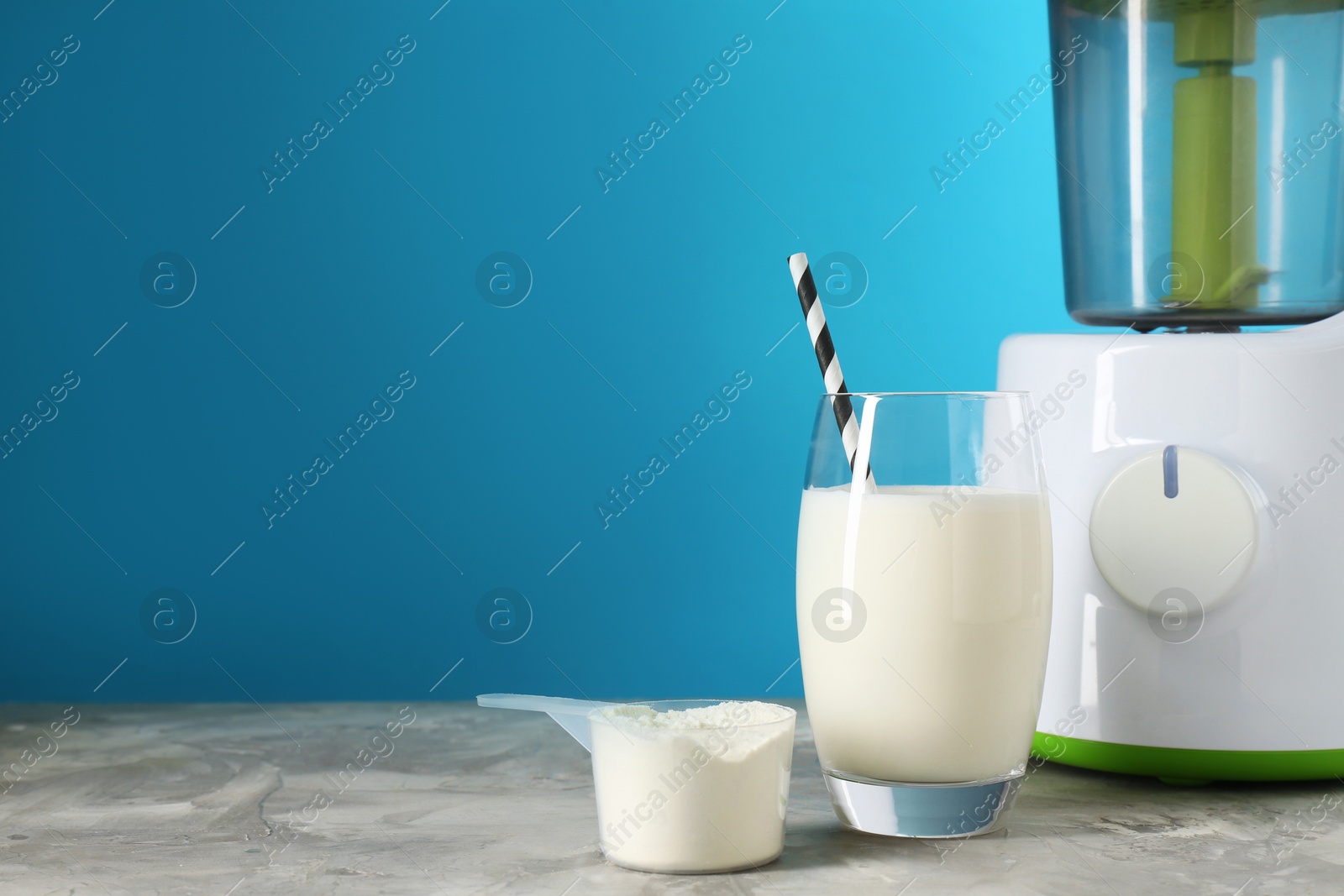 Photo of Blender, delicious protein shake in glass and scoop with powder on gray textured table against light blue background, space for text