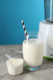 Photo of Delicious protein shake in glass, scoop with powder and blender on gray textured table against light blue background