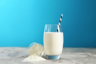 Photo of Delicious protein shake in glass and scoop with powder on gray textured table against light blue background