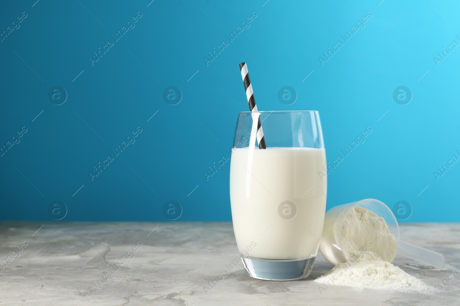 Photo of Delicious protein shake in glass and scoop with powder on gray textured table against light blue background, space for text