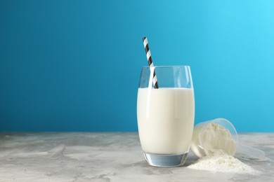 Photo of Delicious protein shake in glass and scoop with powder on gray textured table against light blue background, space for text